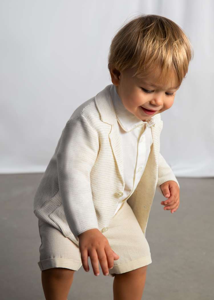 Child wearing a white outfit with a textured pattern on a plain background