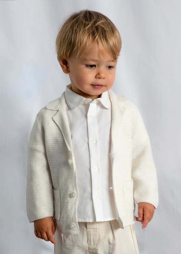 Young child wearing a light-colored jacket over a white shirt on a plain background