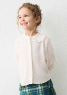 Young girl wearing a white blouse and plaid skirt against a white wall