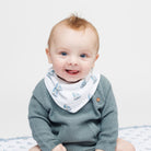 Baby wearing a green sweater and a white bib with blue sailboat pattern on a light gray background