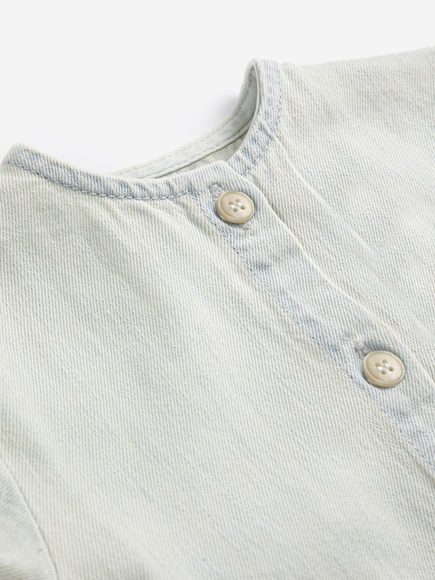 Light blue denim fabric with button details on a white background