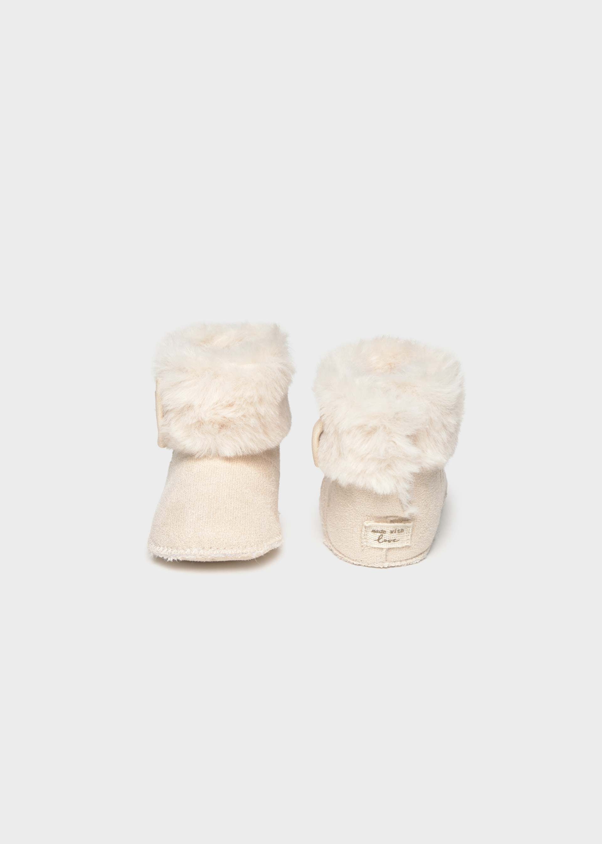 A pair of cream-colored faux fur booties with soft suede-like soles, shown from the back on a light gray background.