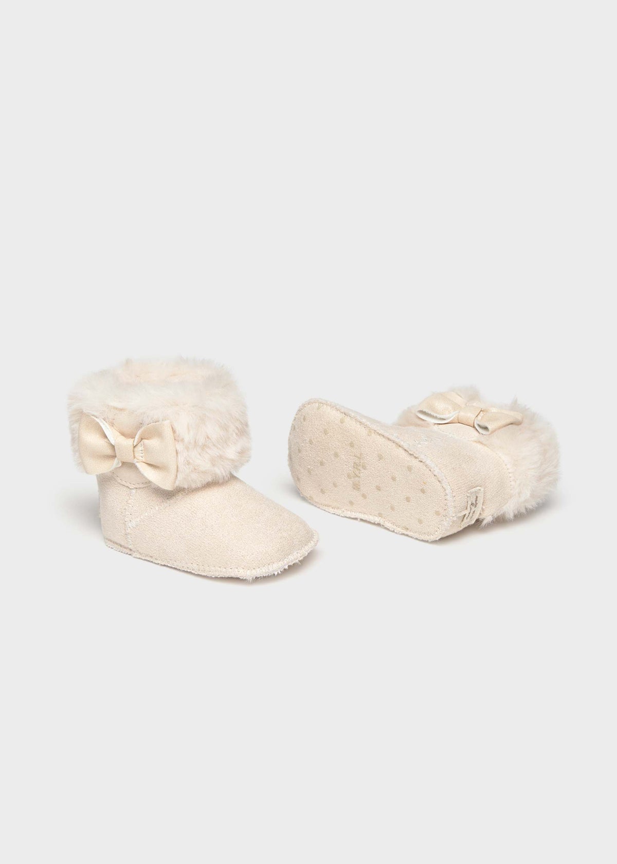 A pair of cream-colored baby booties with fluffy faux-fur trim and bow details, shown on a light gray background.