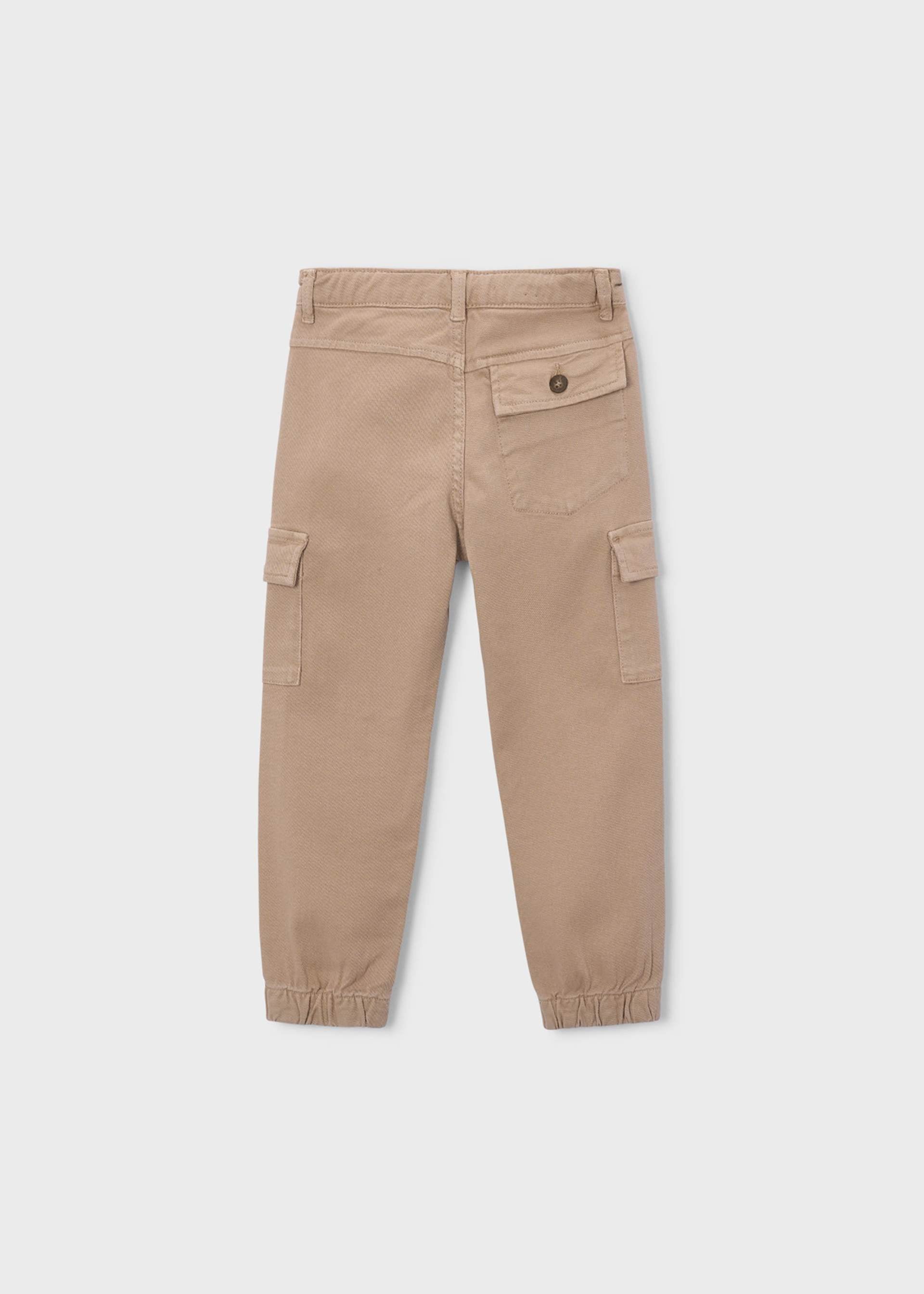 A pair of beige cargo pants shown from the back, featuring a buttoned flap pocket, side cargo pockets, and elasticated cuffs, displayed on a light gray background.