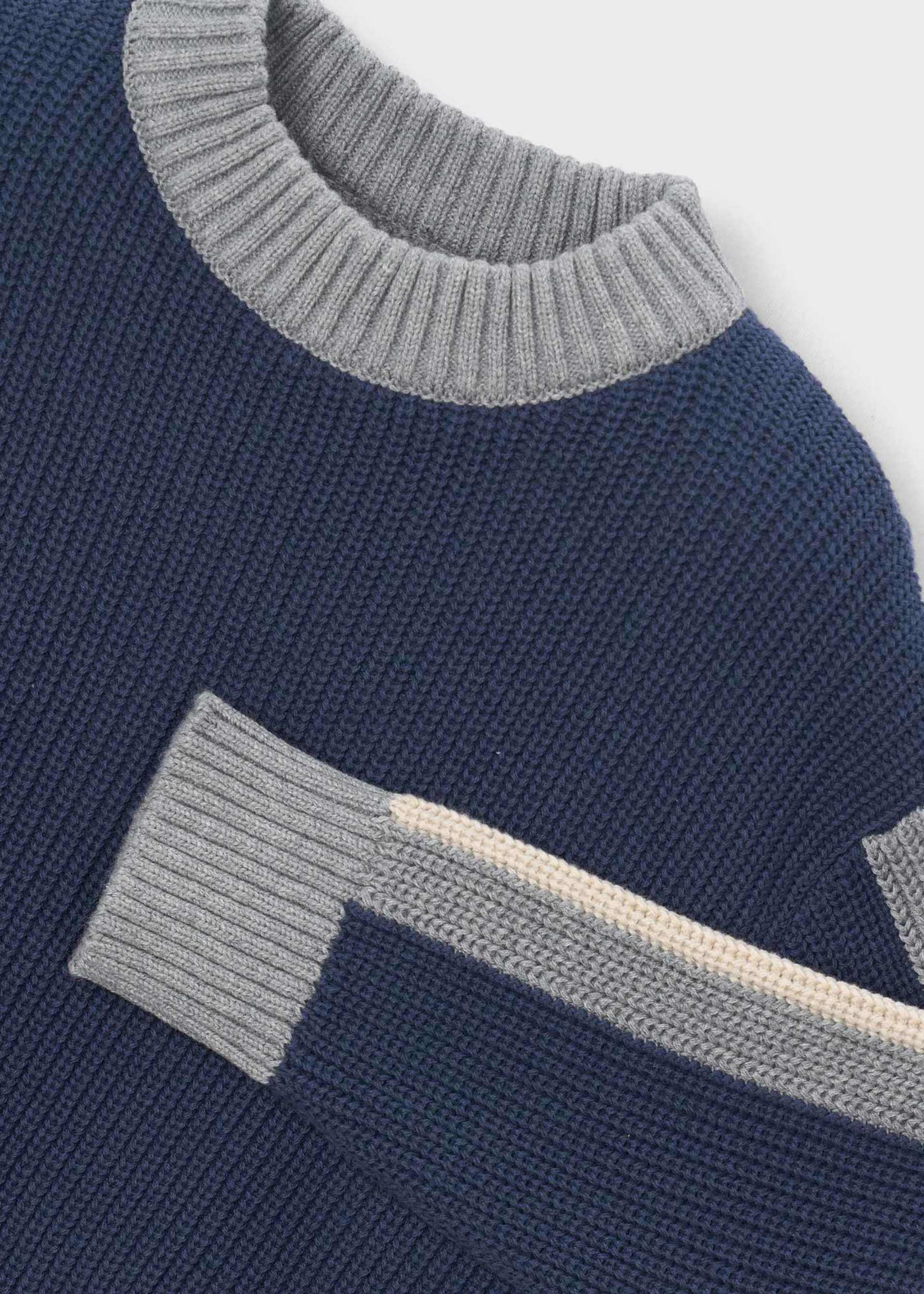 Close-up of a ribbed knit sweater in navy blue with light gray ribbed trim at the crew neck and sleeve cuff, plus a contrasting light beige stripe running diagonally.