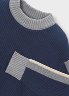 Close-up of a ribbed knit sweater in navy blue with light gray ribbed trim at the crew neck and sleeve cuff, plus a contrasting light beige stripe running diagonally.