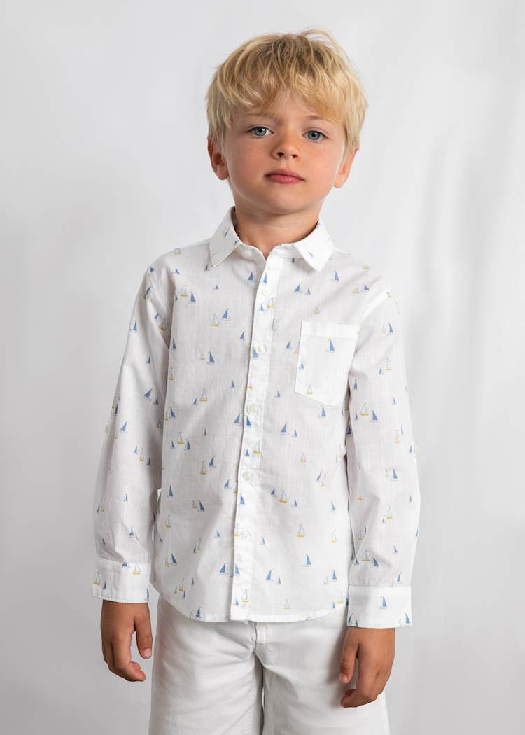 Young boy wearing a white shirt with small patterns and white pants on a plain background