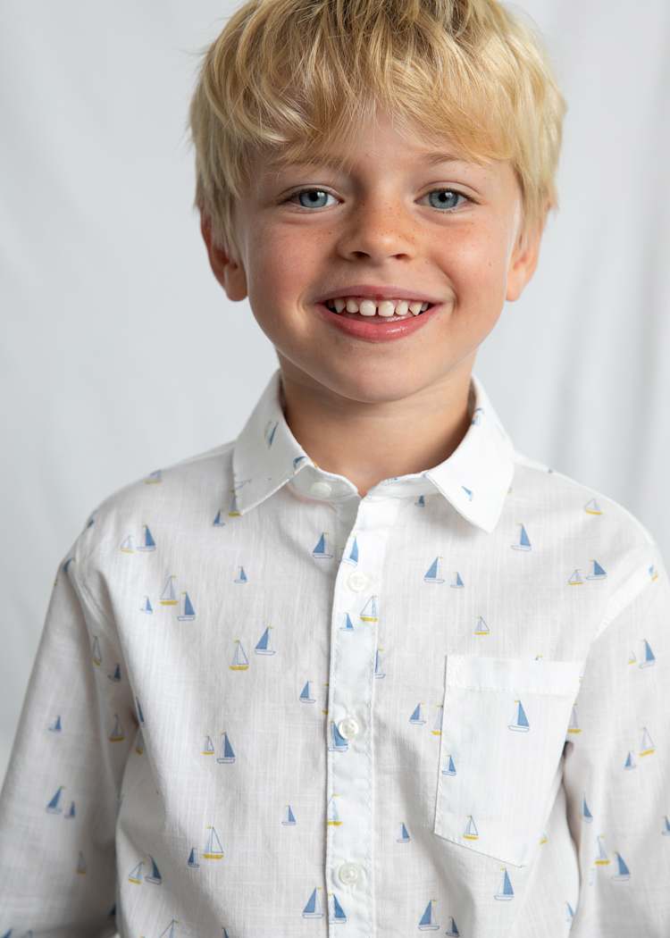 Young boy wearing a white shirt with sailboat pattern against a plain background