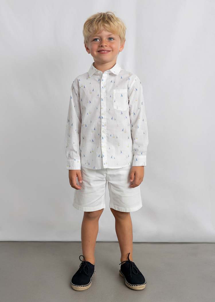 Young boy wearing a white patterned shirt and shorts against a plain background