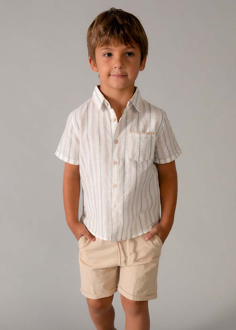 Young boy wearing a striped shirt and beige shorts against a gray background