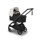 A stroller and bassinet travel system shown on a clean white background. The system features a black stroller base, black wheels, a black handlebar, and a light beige/cream hood and bassinet cover.