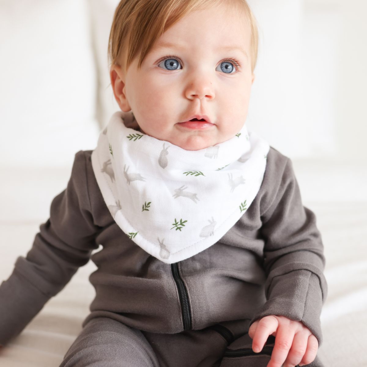 Baby wearing a gray outfit with a white bib featuring green leaf patterns.