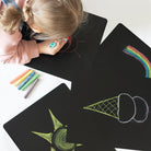 Child drawing on black paper with colorful crayons, surrounded by completed drawings.