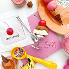 Colorful ice cream-themed party supplies including cones, spoons, and a cherry on top napkin.