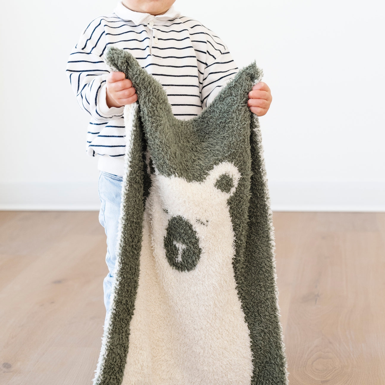 Child holding a soft, plush blanket with a bear design against a plain background