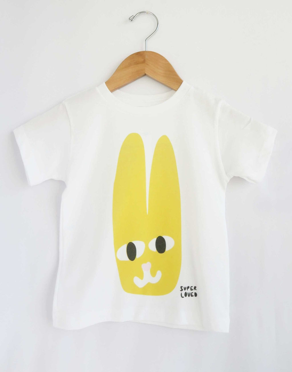 White t-shirt with a yellow cartoon character on a wooden hanger against a white background