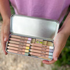 Set of colored pencils in a metal case held by hands against a blurred natural background