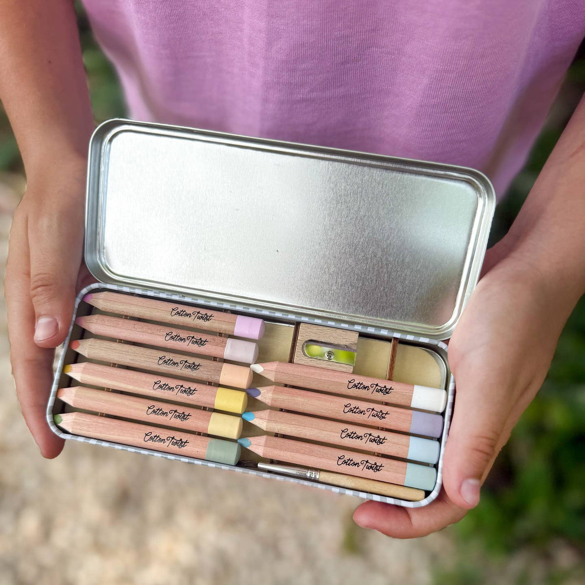 Set of colored pencils in a metal case held by hands against a blurred natural background
