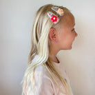 Profile of a child with blonde hair wearing decorative hair clips against a plain background