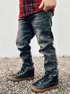 Child wearing black boots and gray jeans on a gravel surface with a blurred background