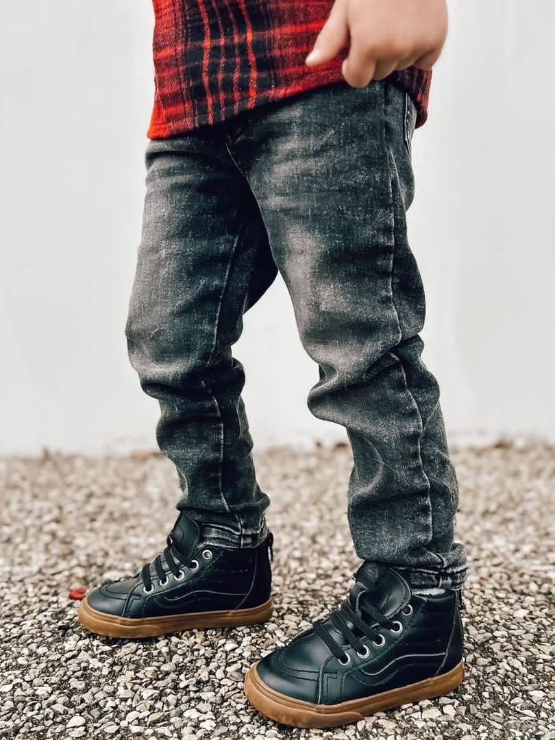 Child wearing black boots and gray jeans on a gravel surface with a blurred background