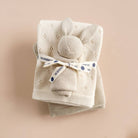 Folded beige baby blanket with a gray ball and blue tag on a beige background