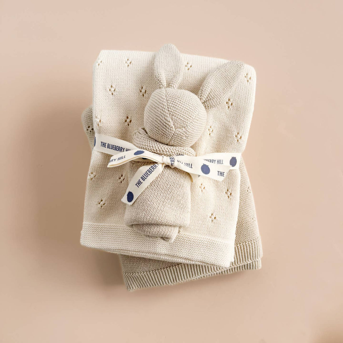 Folded beige baby blanket with a gray ball and blue tag on a beige background