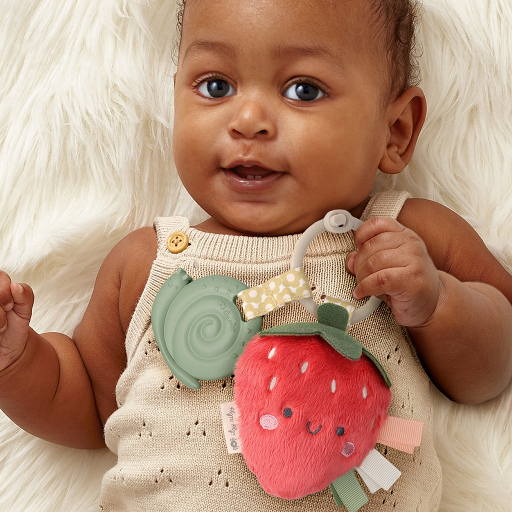 Baby holding a soft toy with a strawberry design on a white fluffy background