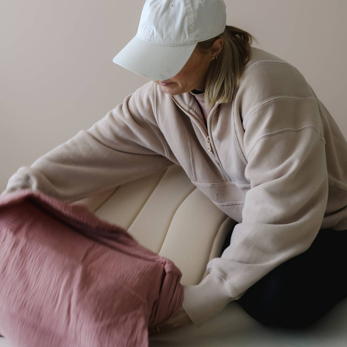 Person sitting on a couch holding a pink blanket against a plain background