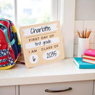 First day of school sign for Charlotte in first grade with backpack and supplies on a desk.