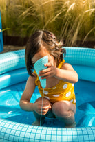 Child playing with a blue toy in a small inflatable pool outdoors.