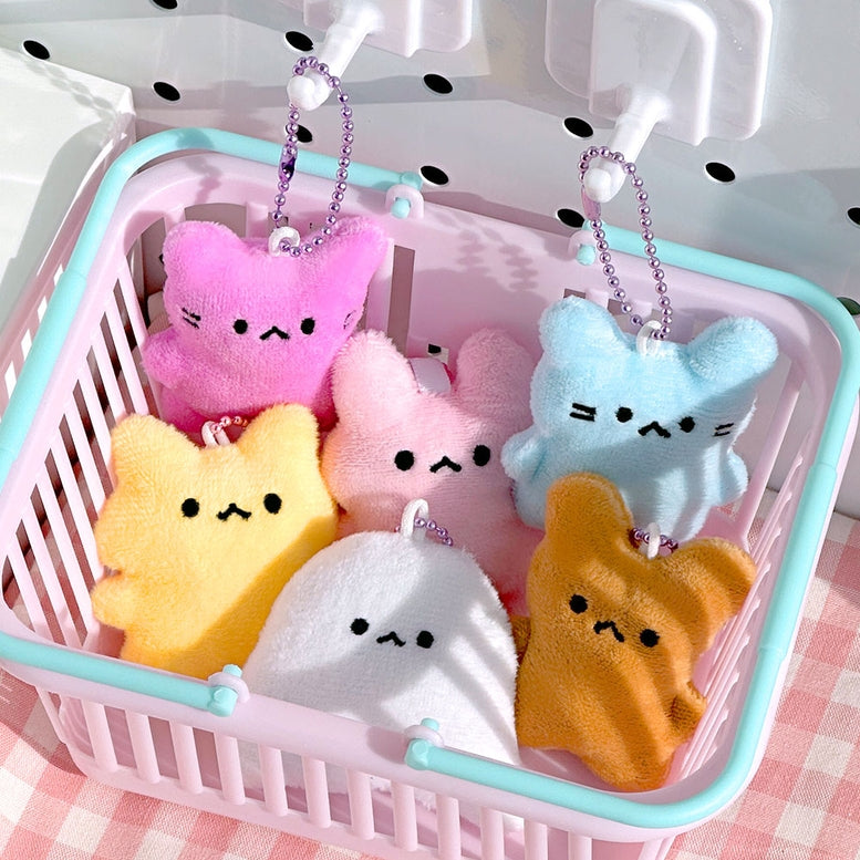 Six small plush character keychains or bag charms in pink, light blue, yellow, white, and orange, hanging from silver chains inside a pastel pink and mint basket.