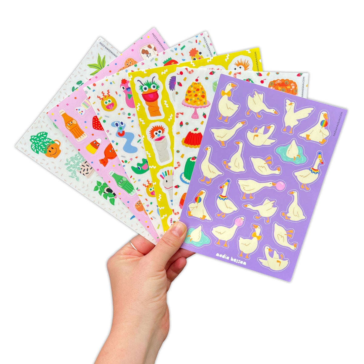 Hand holding a set of colorful sticker sheets with various designs on a white background