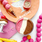 Sundae setup with ice cream, toppings, and pink beads on a white background