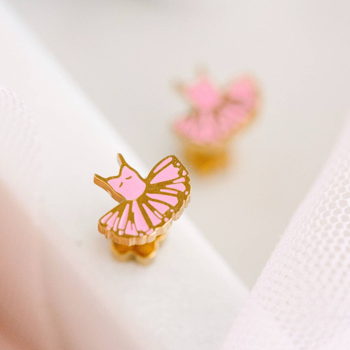 Pink and gold butterfly-shaped earrings on a white background