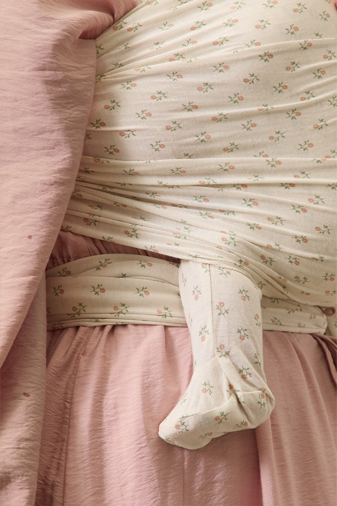 Close-up of a baby in a floral outfit wrapped in a pink blanket