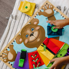 Educational toy board with bear character and various educational elements with hands on a biege background