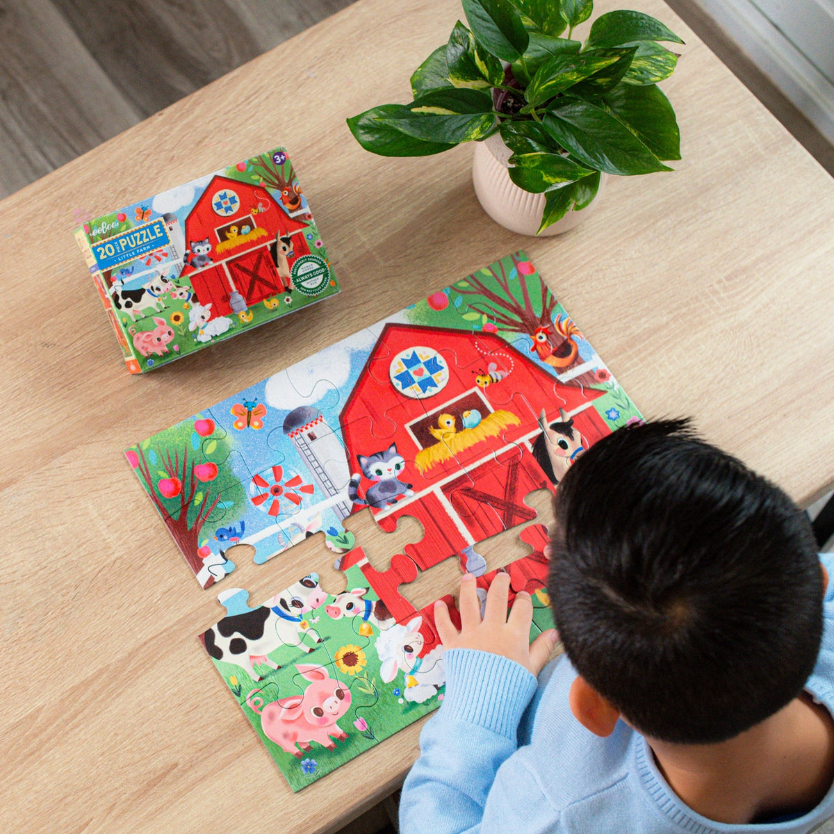 Child playing with a farm-themed puzzle on a wooden table with a plant in the background