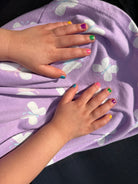 Two hands with colorful nail polish on a purple fabric with butterfly patterns.
