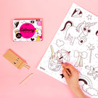 Pencil held by hand coloring a book on a pink background