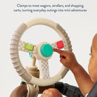 Child's hand interacting with a toy steering wheel attached to a stroller, with text about clamping to wagons and strollers.