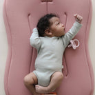 Baby lying on a pink cushion with a pacifier nearby