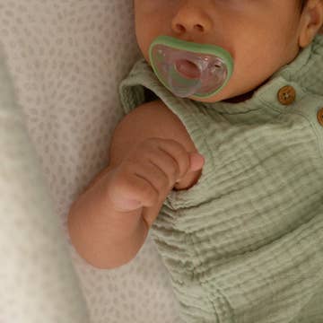 Baby wearing a green outfit with a pacifier, lying on a textured surface.