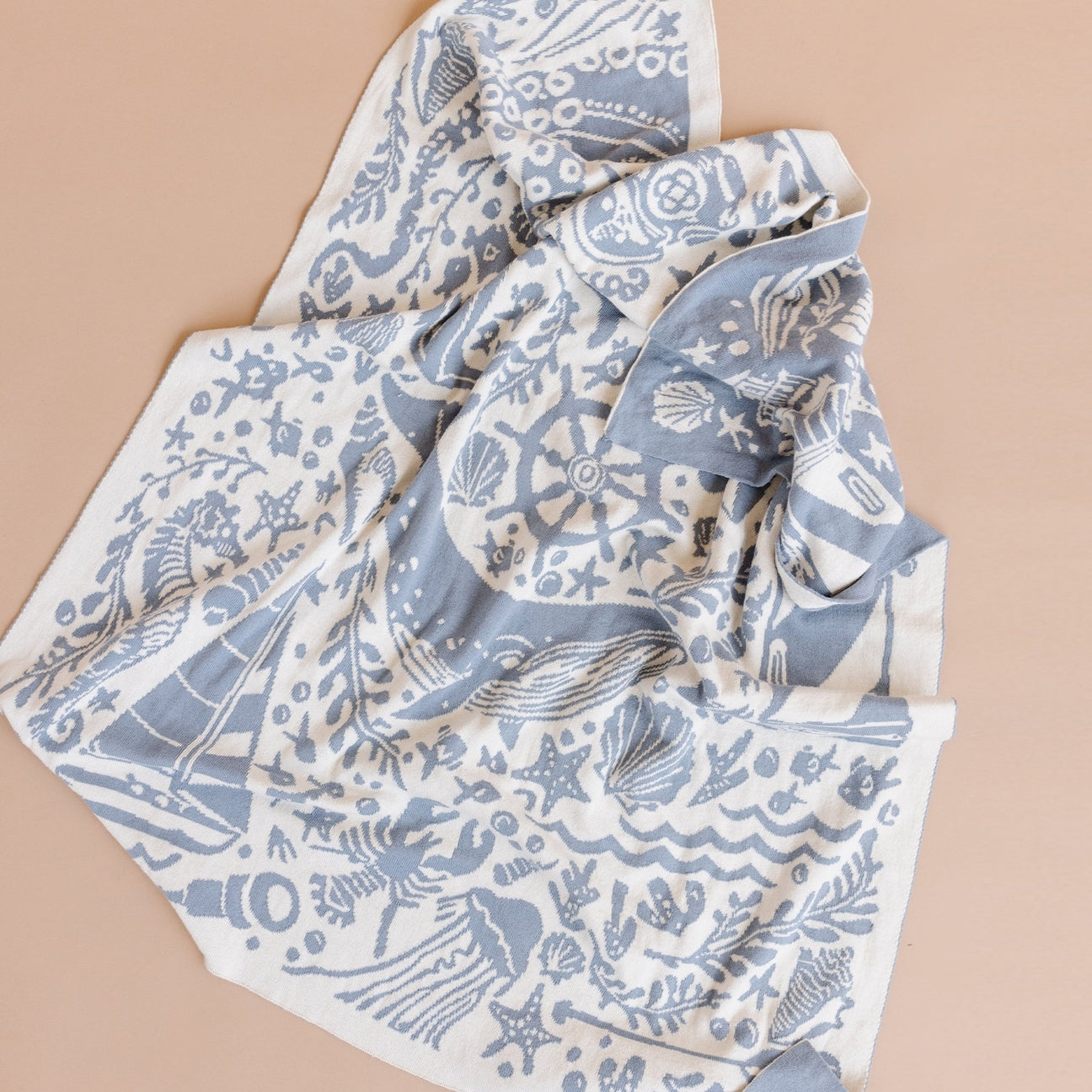 A lightweight square scarf with a blue and white nautical print, featuring illustrations of sea creatures, waves, and a ship's wheel, laid out on a solid beige background.