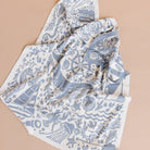 A lightweight square scarf with a blue and white nautical print, featuring illustrations of sea creatures, waves, and a ship's wheel, laid out on a solid beige background.
