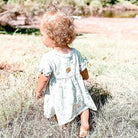 Child in a light dress standing in tall grass with a natural background