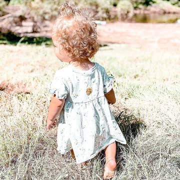 Child in a light dress standing in tall grass with a natural background