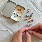 Colorful beads and letter beads on a textured surface with hands holding a letter bead.