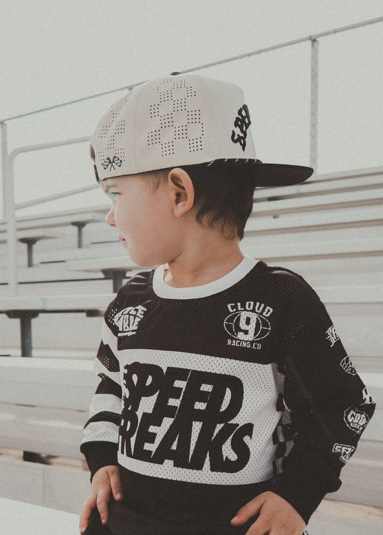 Child wearing a black and white outfit with 'Speed Freaks' text, standing on bleachers.
