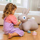 Child playing with a large plush rabbit toy on a wooden floor.